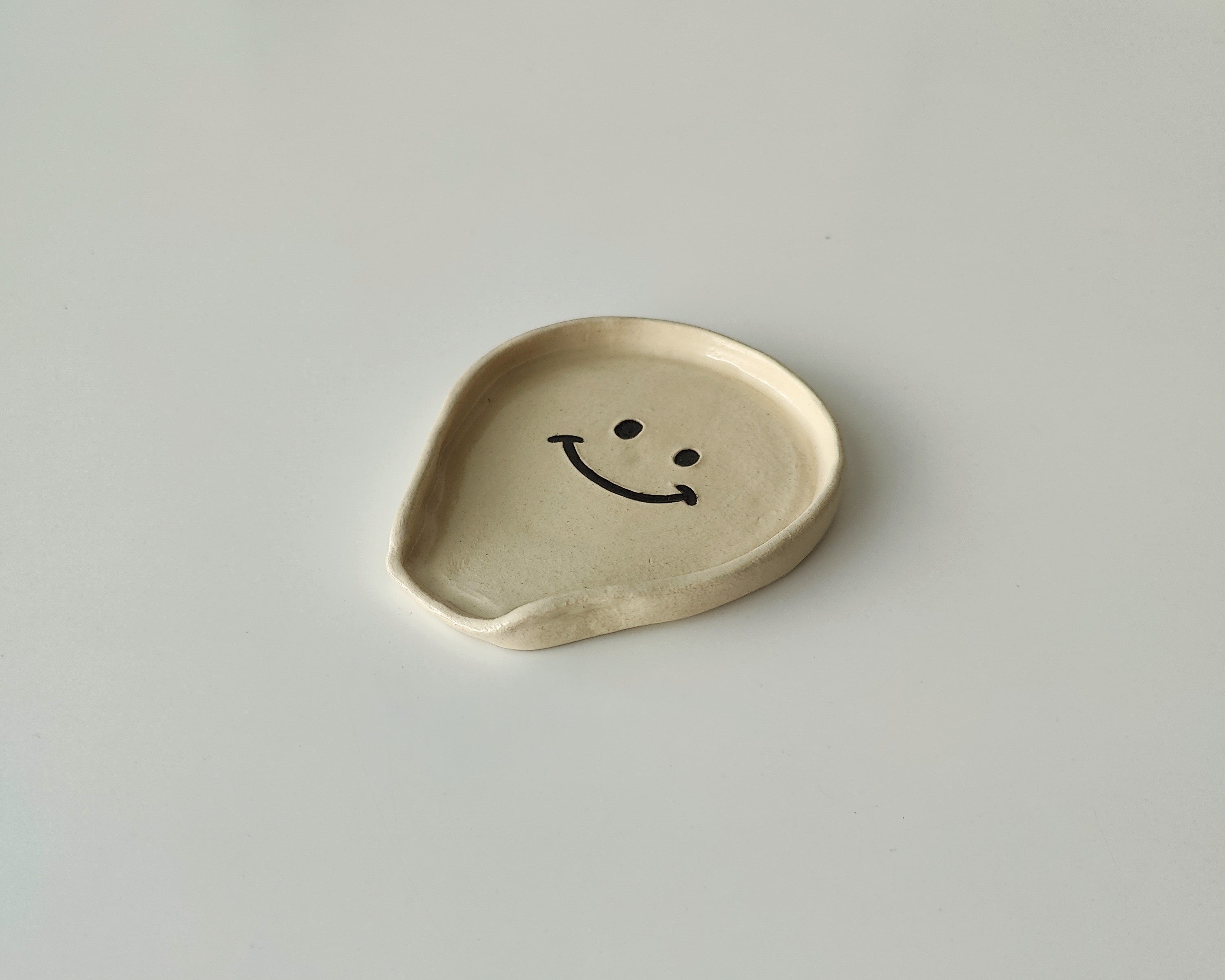 Keraaminen kauhalautanen, jossa on musta hymyilevä emoji keskellä.